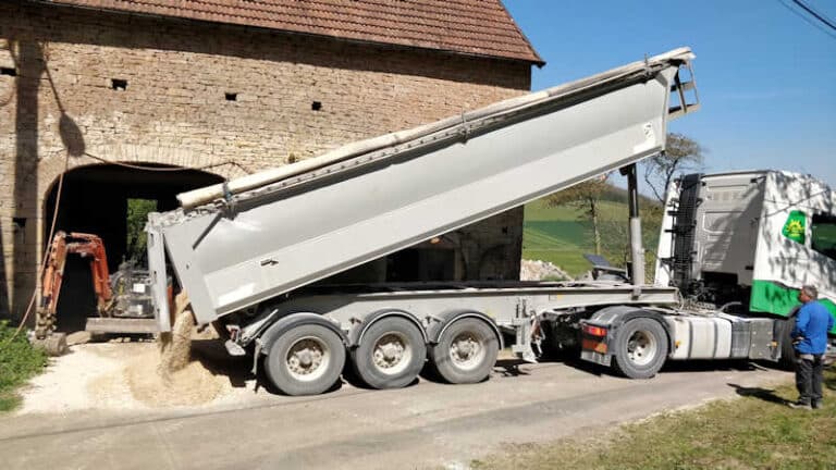 Vrachtwagens vol met fijn gravel voor over het puin